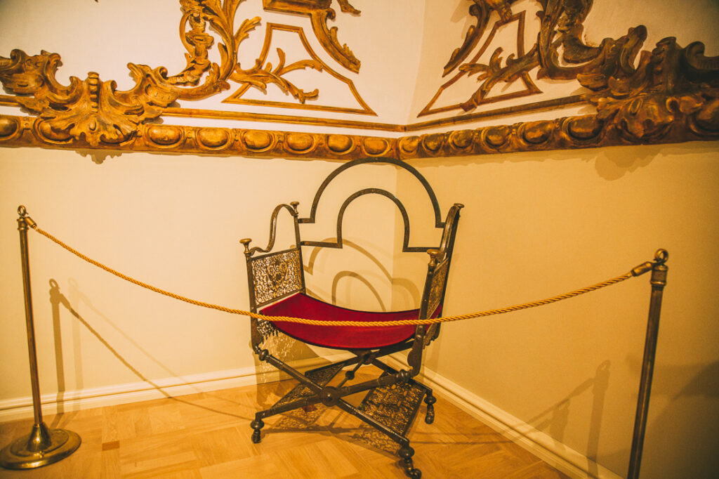 Elizabeth's traveling chair on display behind ropes inside Catherine Palace.