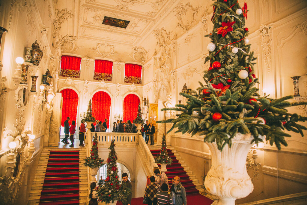 The grand entrance at Catherine Palace with two staircases filled with filing tourists, and a Christmas floral arrangement at the forefront of the photo.