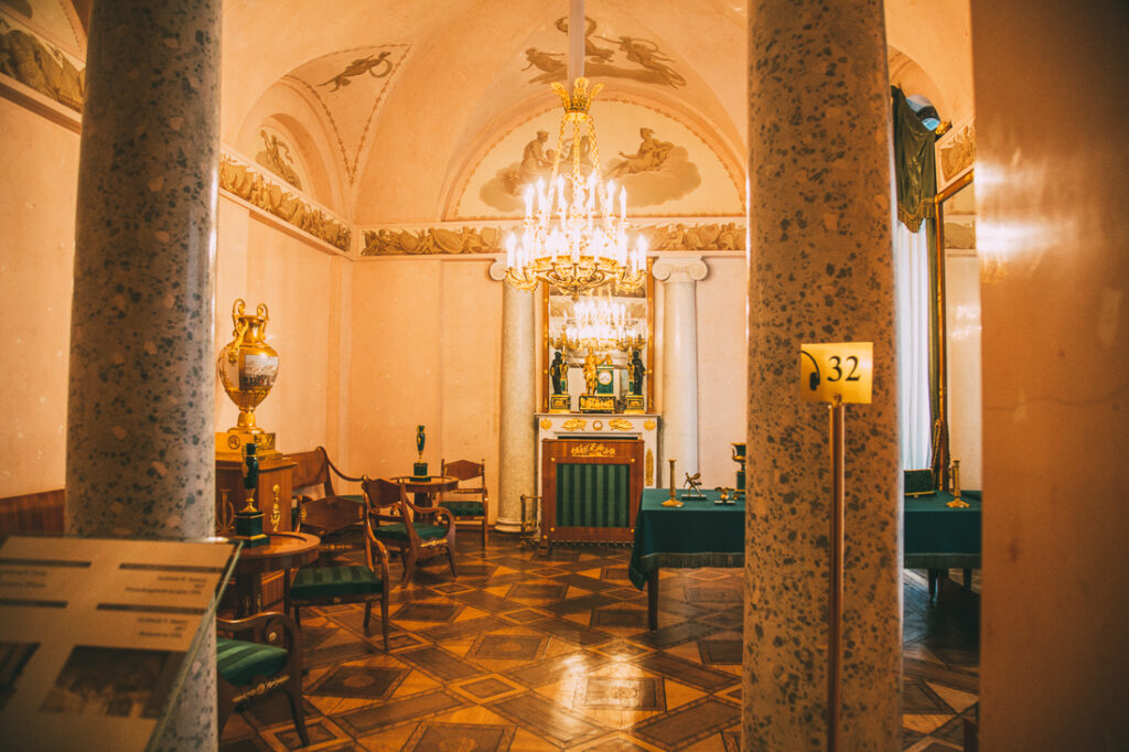 A large entrance hall inside Catherine Palace with parquet wood floors, stone pillars, arched ceilings, and gold crown molding.