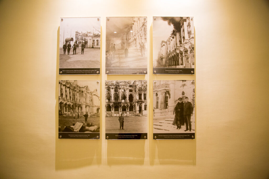 A display of six black and white photos hang on a white wall, depicting scenes of Catherine Palace before it was restored.
