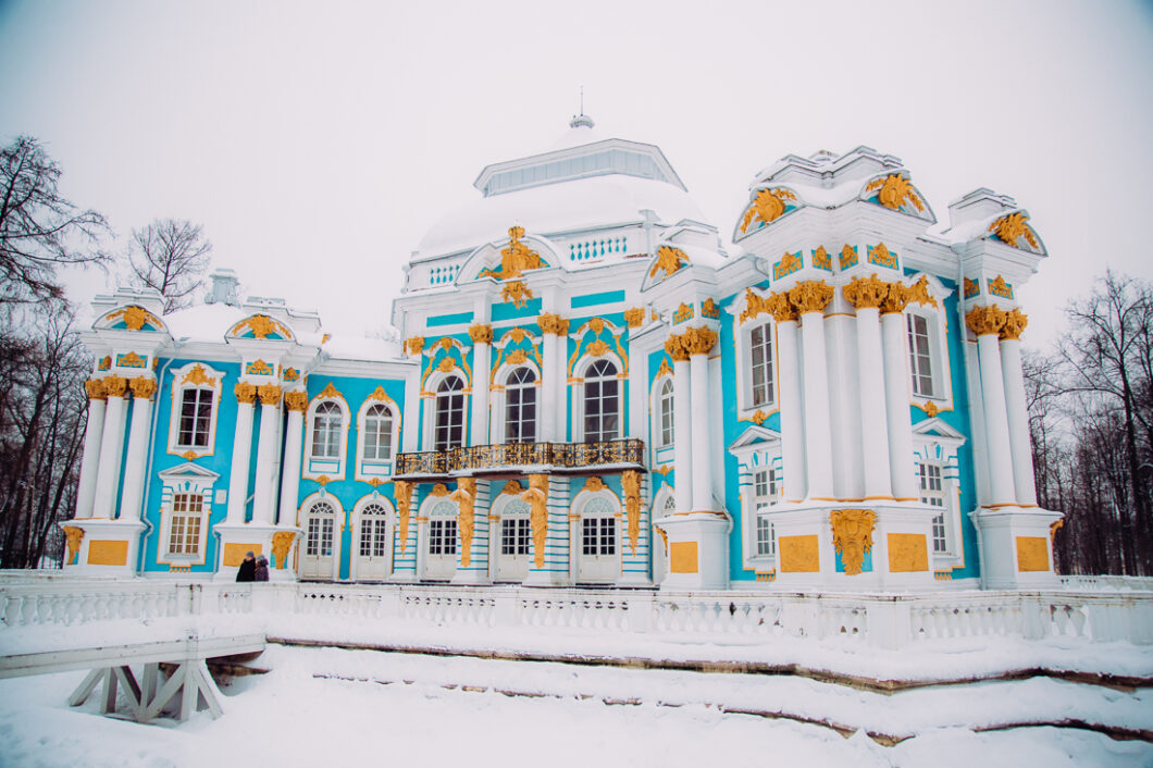 The exterior of The Hermitage near Catherine's Palace in St. Petersburg Russia. The building has a white and turquoise exterior with elegant gold molding.