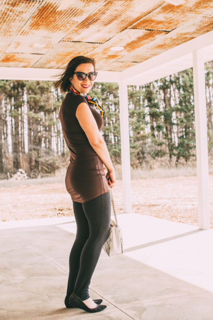 beautiful women saying in fitted T-shirt with scarf, sunnies, black pants, holding a white bag and black pumps shoes