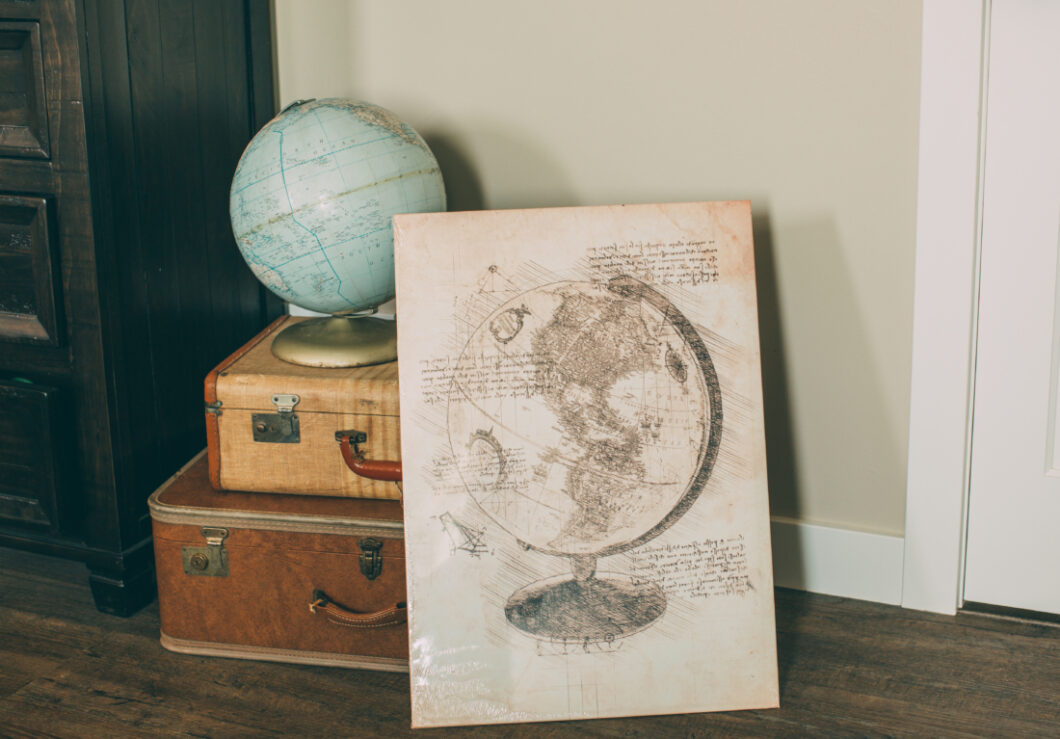 A vintage style metal posted of a world globe, propped up against vintage suitcases.