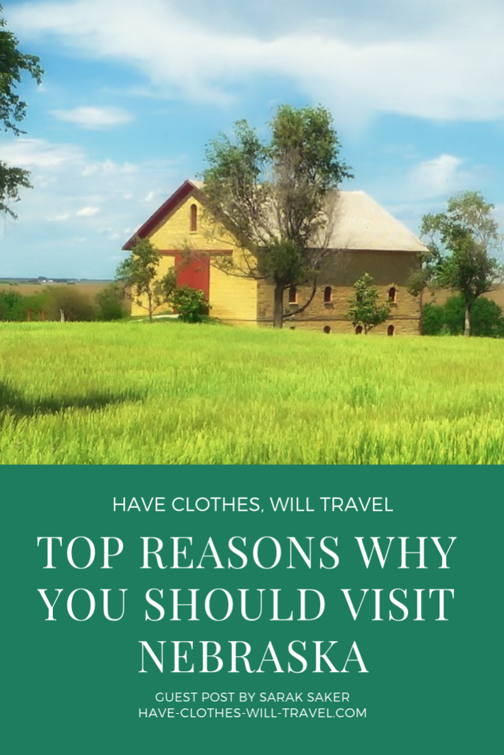 An image of a yellow barn with a red door, standing in a picturesque grass field against a pure blue sky. Text across the bottom of the image reads "top reasons why you should visit Nebraska" in white font on a green background.