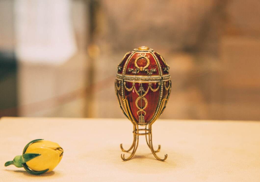 A small red and gold Fabergé egg sits on a gold stand.