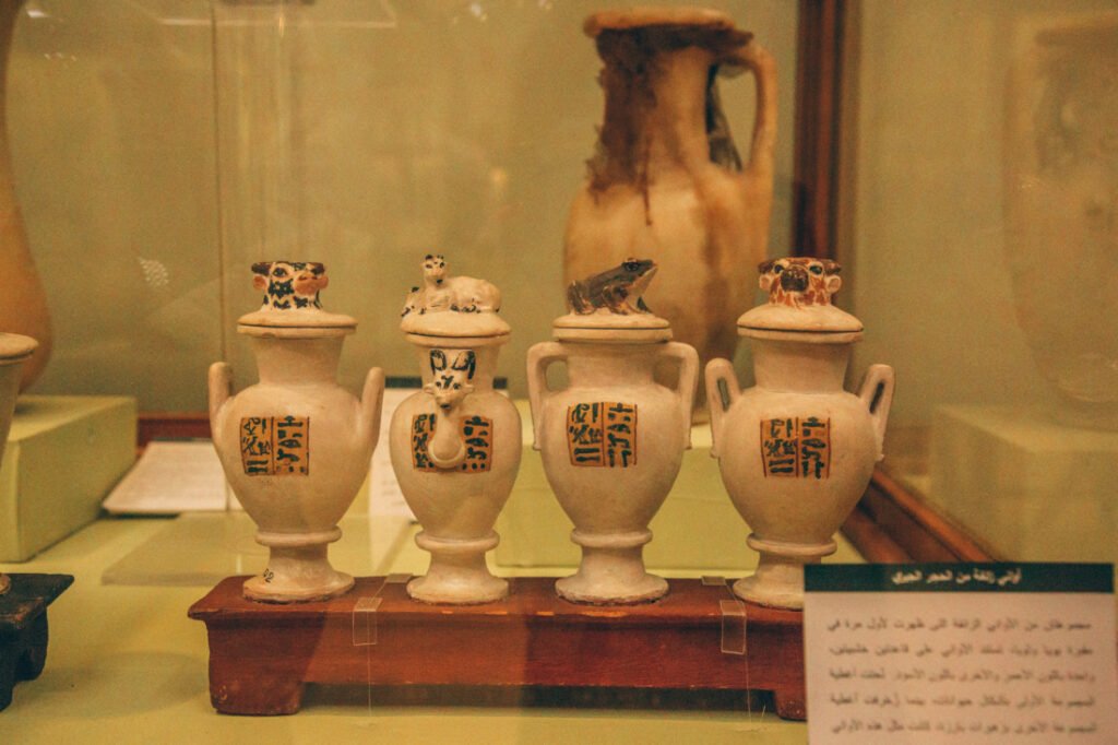 Four white stone-carved jugs with ancient Egyptian writings sit inside a glass display case. 