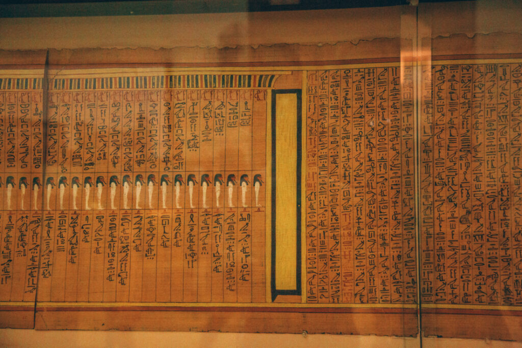 Ancient Egyptian papyrus scrolls feature  thousands-years-old writing, displayed behind a glass case.