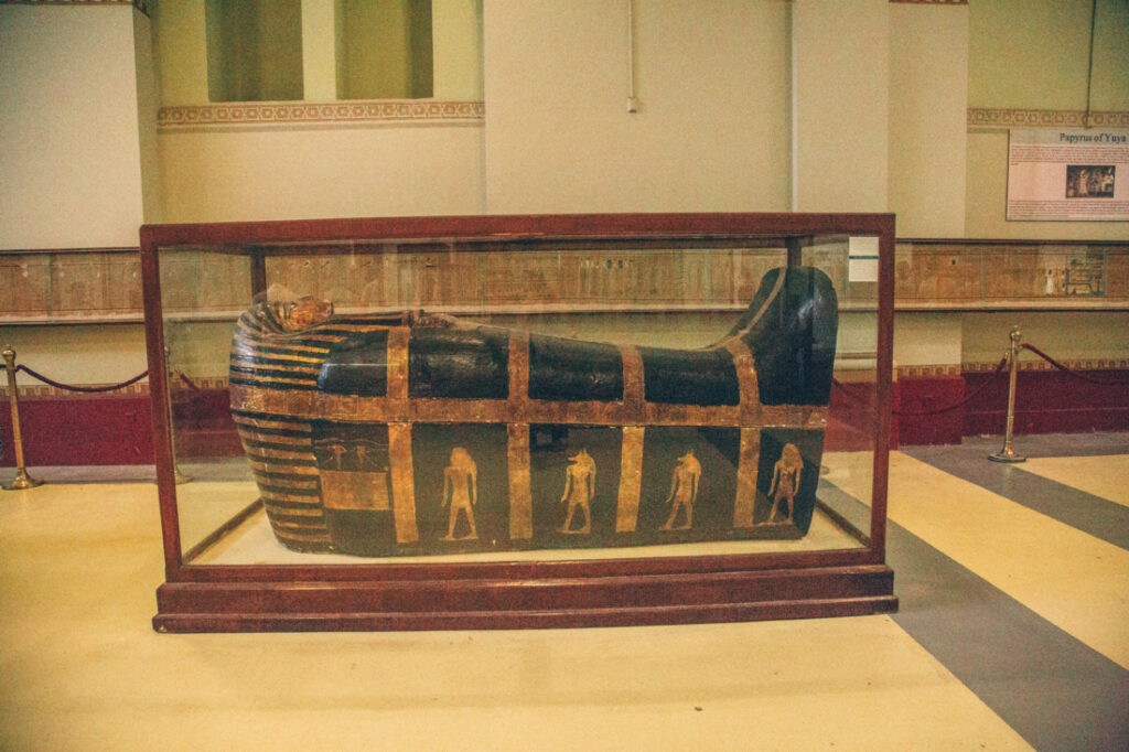 A large black sarcophagus with detailed gold inlays sits inside of a wood-framed glass display case at the Egyptian Museum.