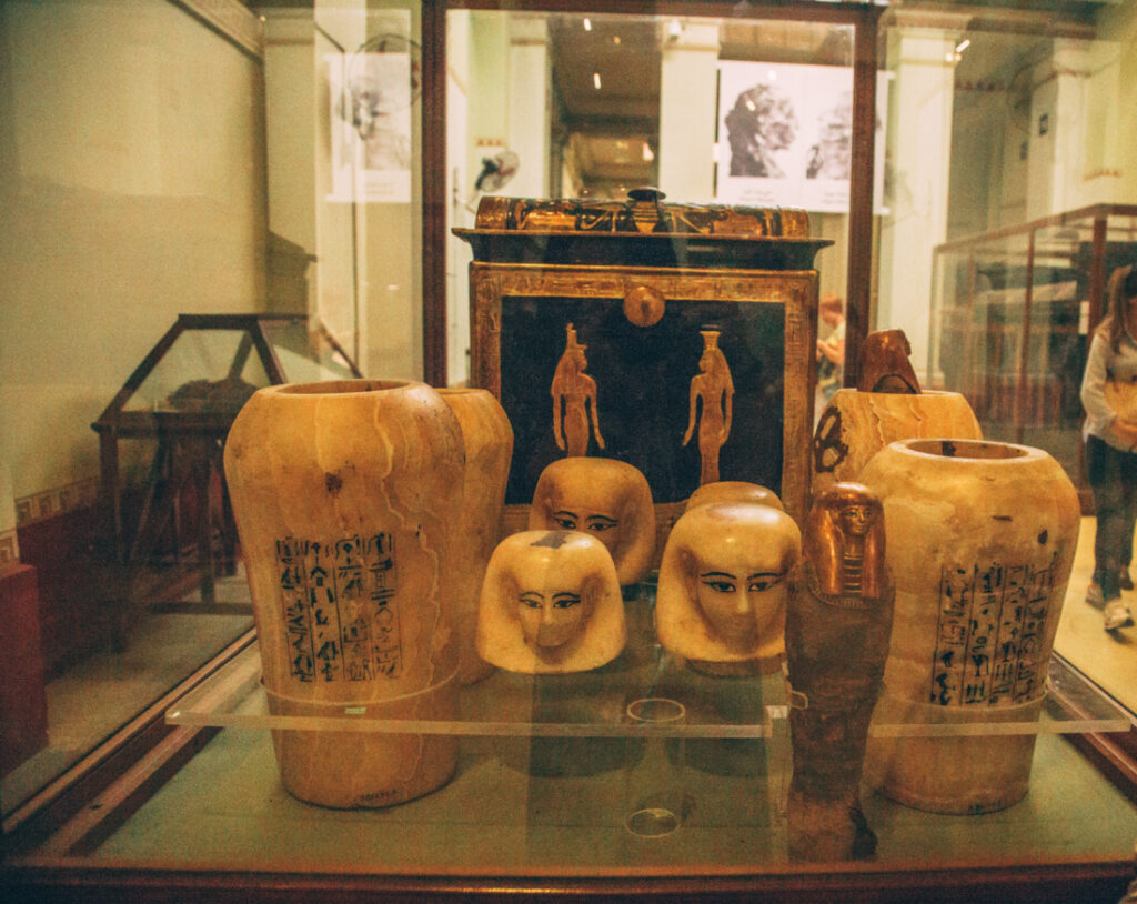 More stone-carved canopic jars displayed with their storage boxes inside a glass case.