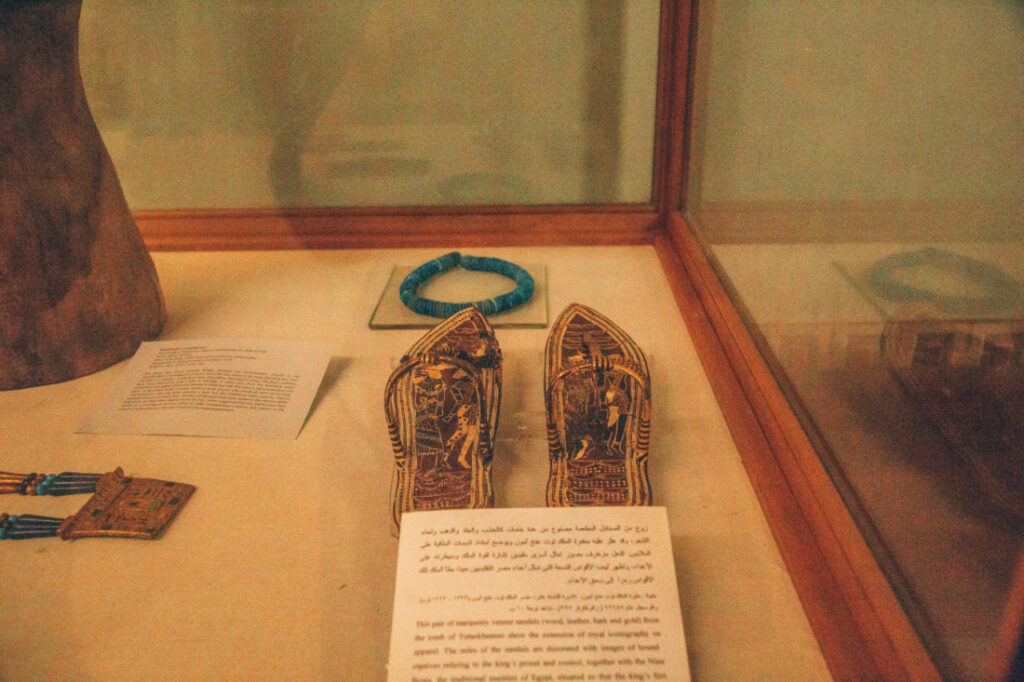 An ancient pair of King Tut's Sandals, displayed with a white information card with Egyptian and English writing.