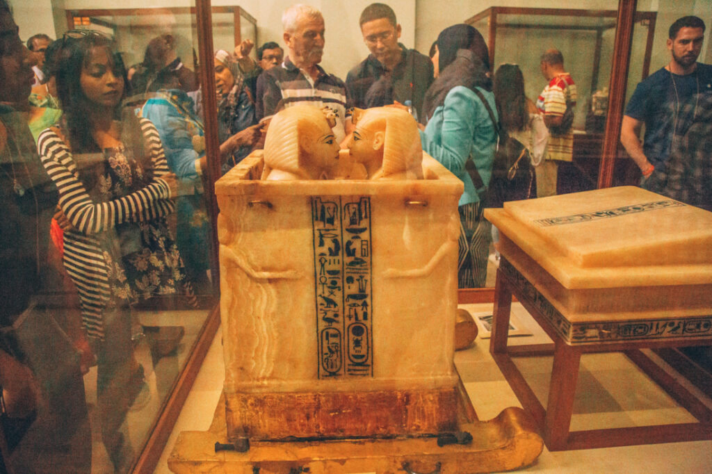 King Tut's canopic jars sit inside a large marble box with a lid, adorned with hieroglyphs along the side of the box. 