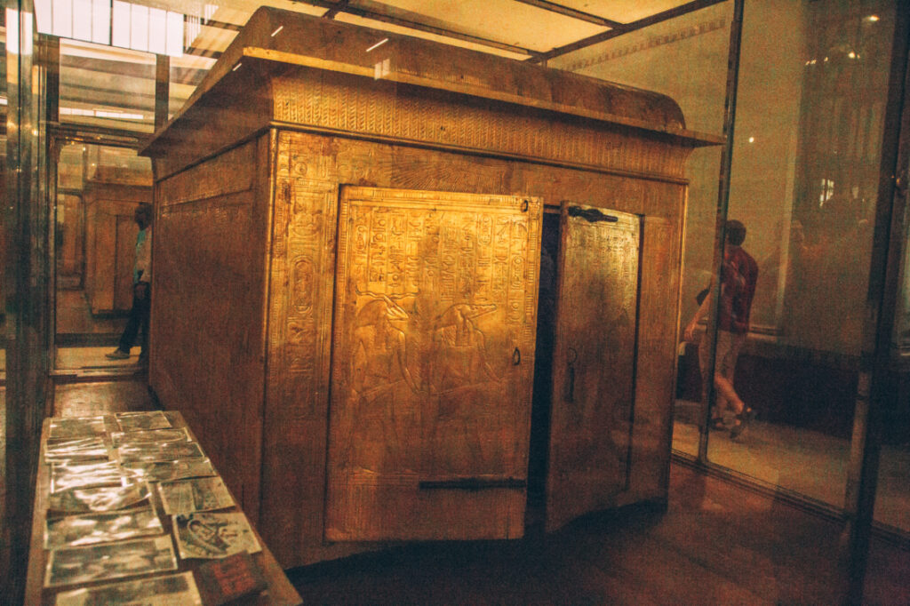 A close up look at the ornate carvings in the doors of one of King Tut's burial sarcophaguses, which is painted gold and displayed inside a glass case.