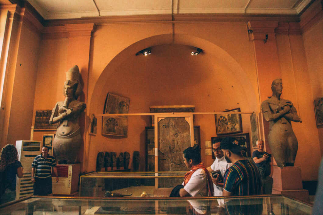 One of the many exhibits inside the Egyptian Museum in Cairo features two large statues on either side of an arched alcove. Glass display cases hold ancient artifacts and artwork hangs on every wall.