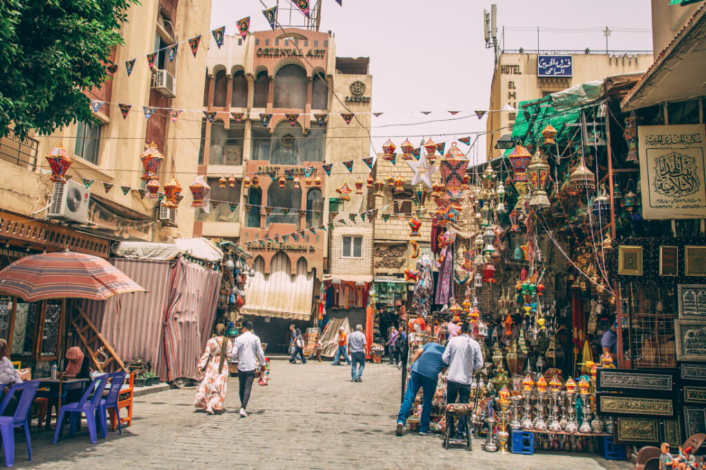 Khan El Khalili Bazaar - a street market lined with stalls selling souvenirs, artifacts, artwork, and more. Banners of flags zig-zag between the stalls that line the streets.