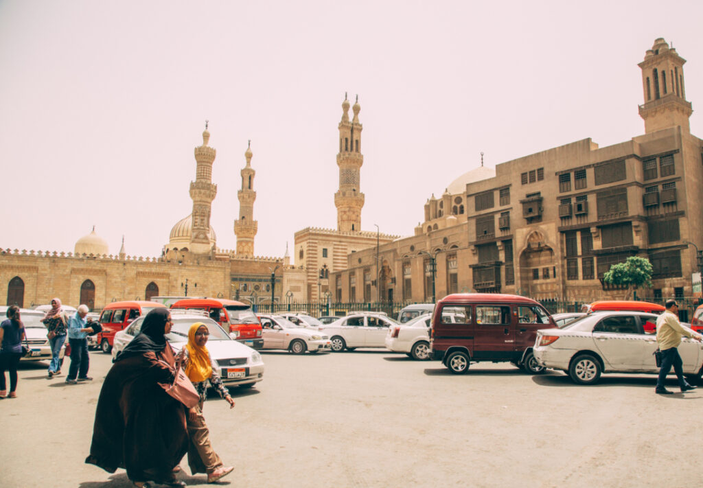 A car park in front of Egyptian buildings, and tourists mulling about on cobblestone streets.