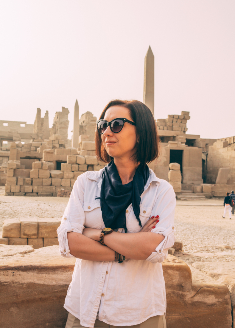 A woman with short brunette hair wearing a white shirt and a black Egyptian cotton scarf around her neck at Karnak Temple in Egypt.