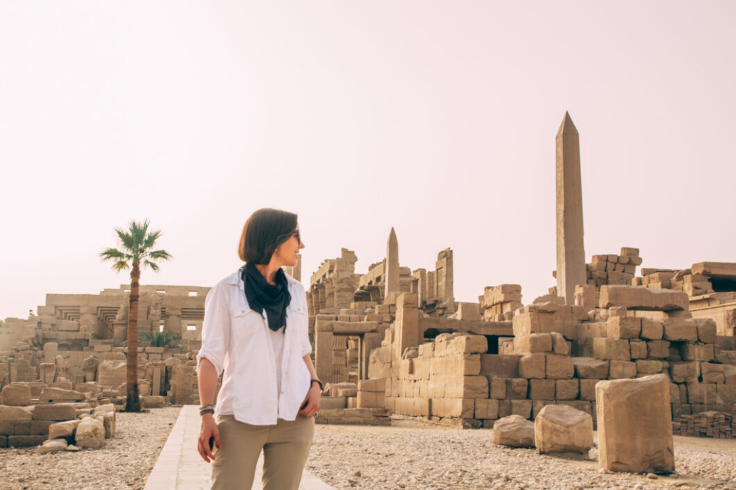 Lindsey of Have Clothes, Will Travel wearing a white linen top and hiking pants at Karnak Temple in Egypt.