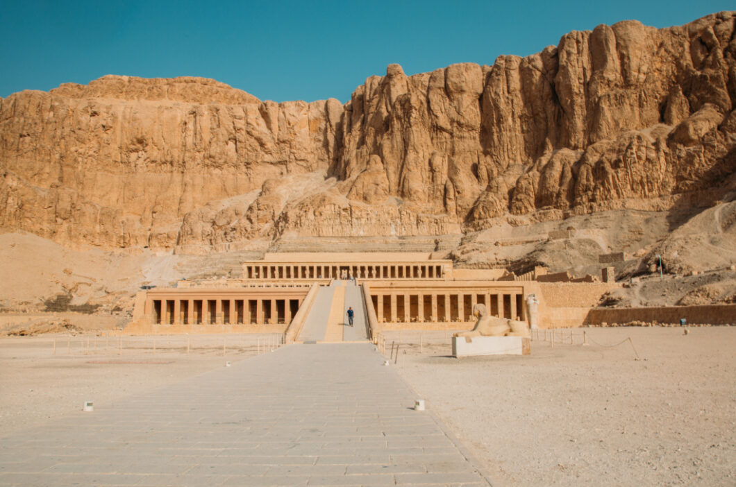 The Temple of Hatshepsut sits at the base of a large desert canyon, surrounded by sandy desert cliffs and hills.