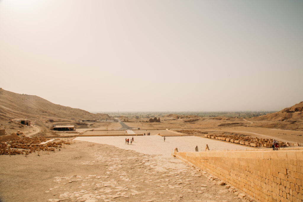 A panoramic landscape shit of Luxor, Egypt with clear, sunny skies, hills, building ruins, and tourists walking around.