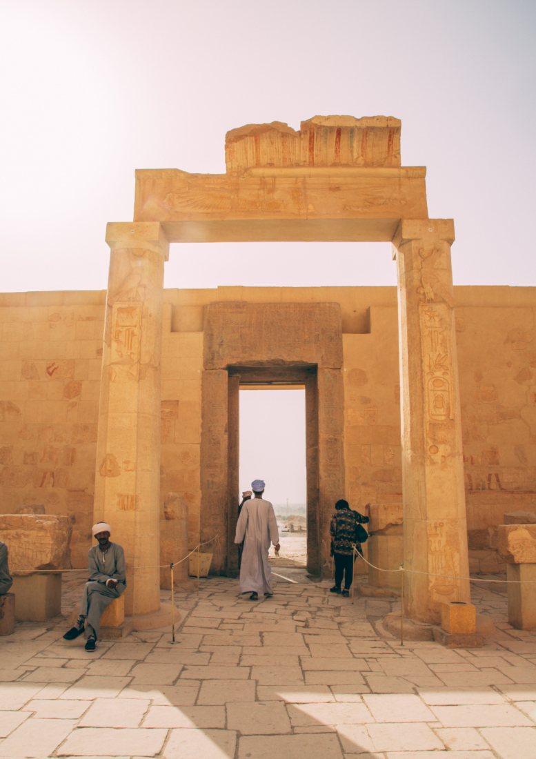 A stone archway outside of the Temple of Hatshepsut near Luxor, Egypt. Locals and tourists walk though the arches as they tour the temple.