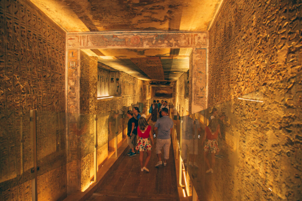 Tourists fill down the lit hallways of a tomb in the Valley of the King, admiring the art-adorned walls protected by glass panels.