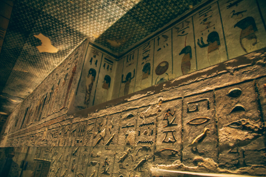 The tall walls and ceilings of a tomb deep under the Valley of the Kings. The stone walls are adorned with hieroglyphs carvings and artwork.