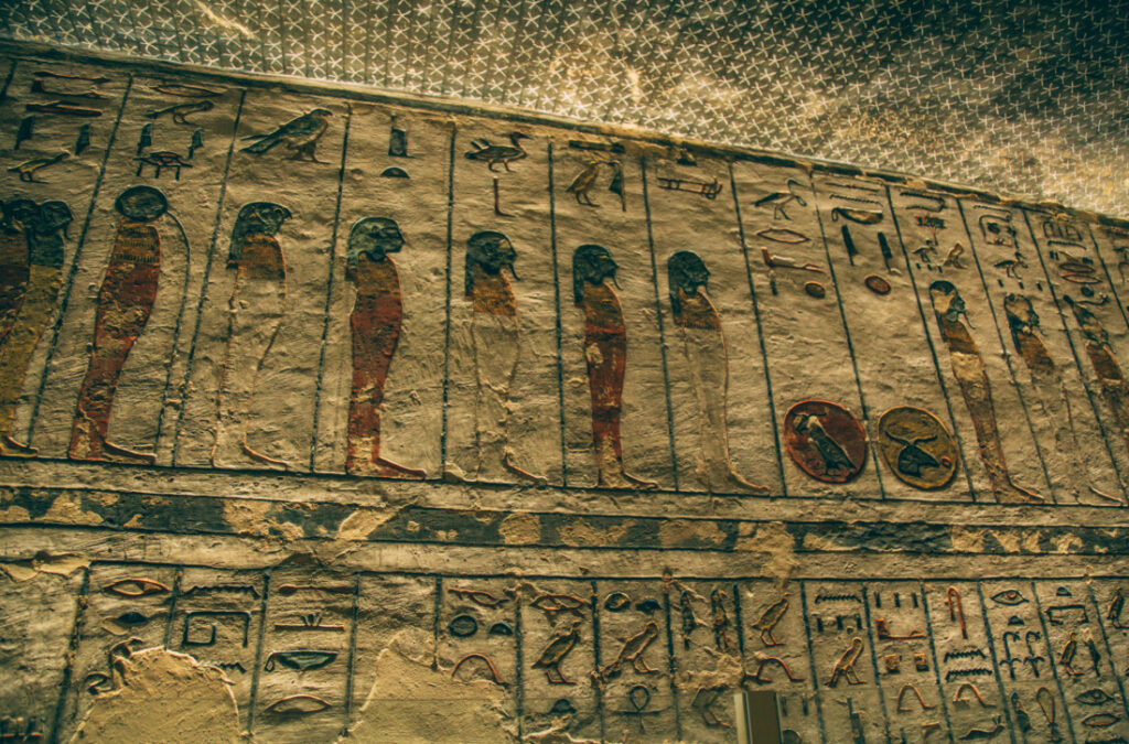 A stone wall and ceiling inside an Egyptian tomb in the Valley of the kings, covered in ancient artwork and hieroglyphs.