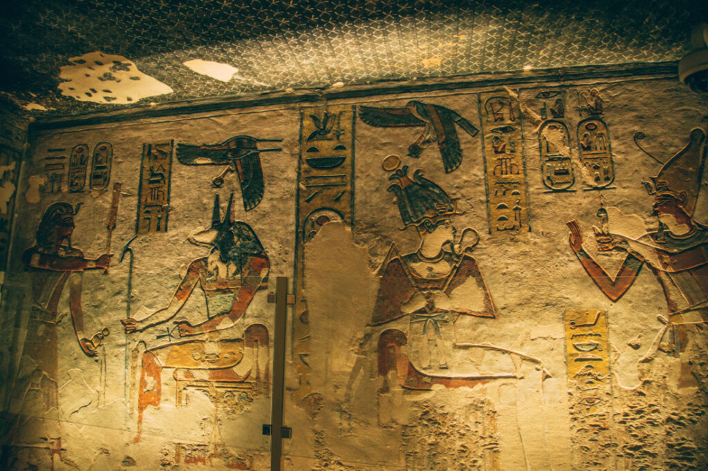 A dimly lit wall inside an ancient Egyptian tomb covered with well-preserved artwork and hieroglyphs.