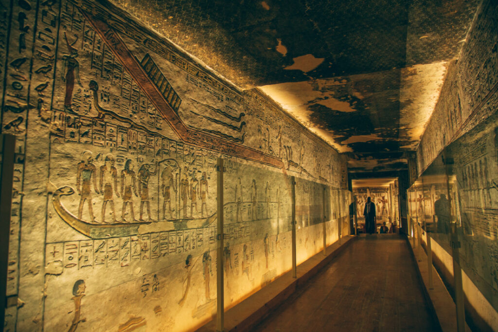 Walls of artwork down a hallway are protected by glass barriers. Tourists view the ancient carvings on the far end of the hallway.