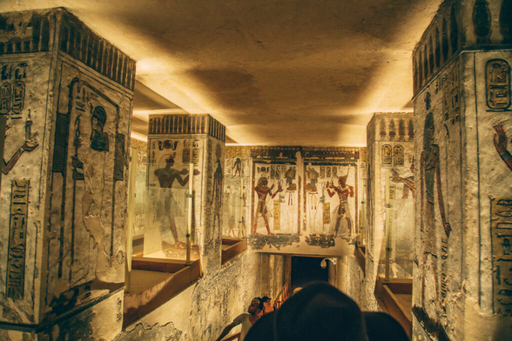 Artwork lines the stone walls of a hallway inside a tomb in the Valley of the Kings. Tourists file down the narrow hallway.