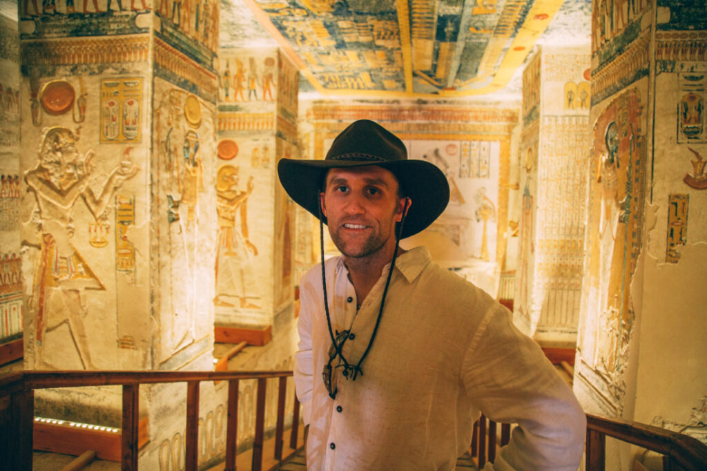 A man wearing a white linen shirt and black hat poses inside a tomb in the Valley of the kings.