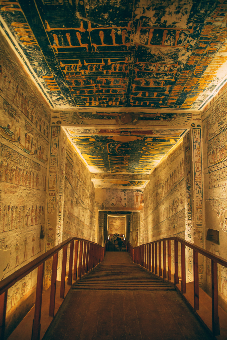 A photo of an underground hallway inside the tomb of King Ramses V. The stone walls and ceiling are completely covered in ancient Egyptian carvings.