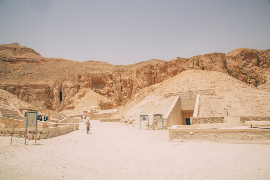 Inside the Valley of the Kings. The landscape of tall desert mountains loom in the background of burial tomb entrances in a sandy desert.
