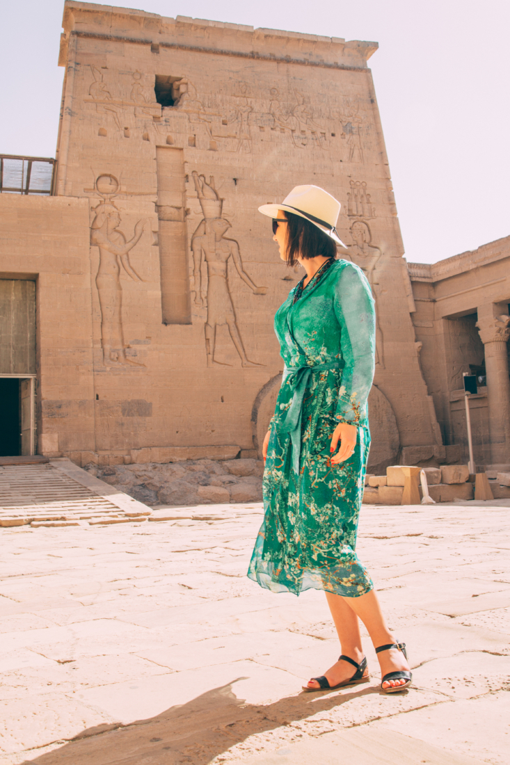 A woman wearing a blue dress and hat in front of an Egyptian temple in Aswan.