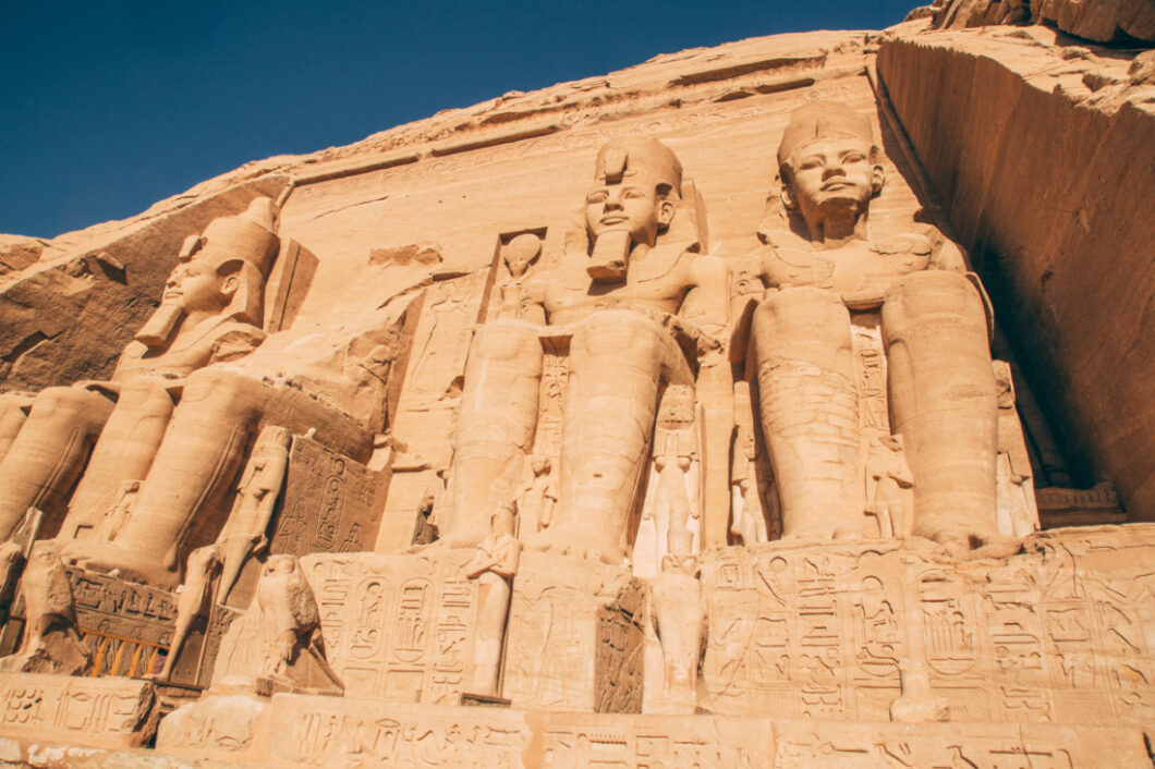 Four giant statues of Ramses II carved from rock into the side of a large mountain temple. The statues surround the entrance to the Ramses temple at Abu Simbel.
