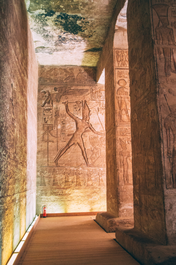 A photo of the tall walls inside one of the Abu Simbel temples. The stone walls and pillars are covered floor to ceiling in ancient Egyptian carvings and artwork.
