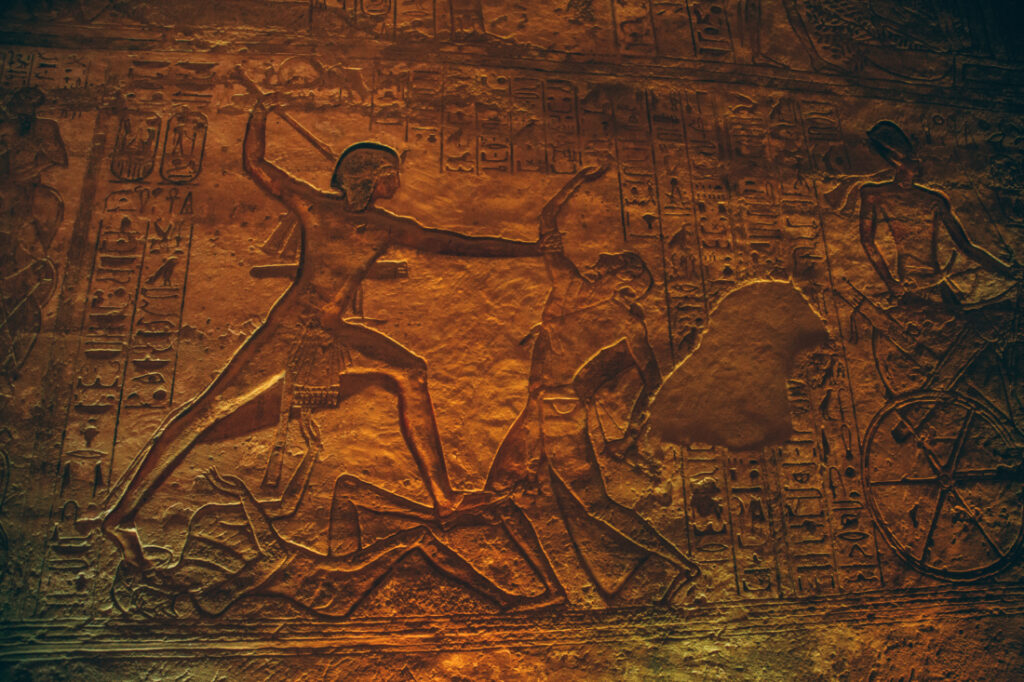 More ancient Egyptian artwork carved into the stone walls of a Abu Simbel temple. This wall is dark and dimly lit.