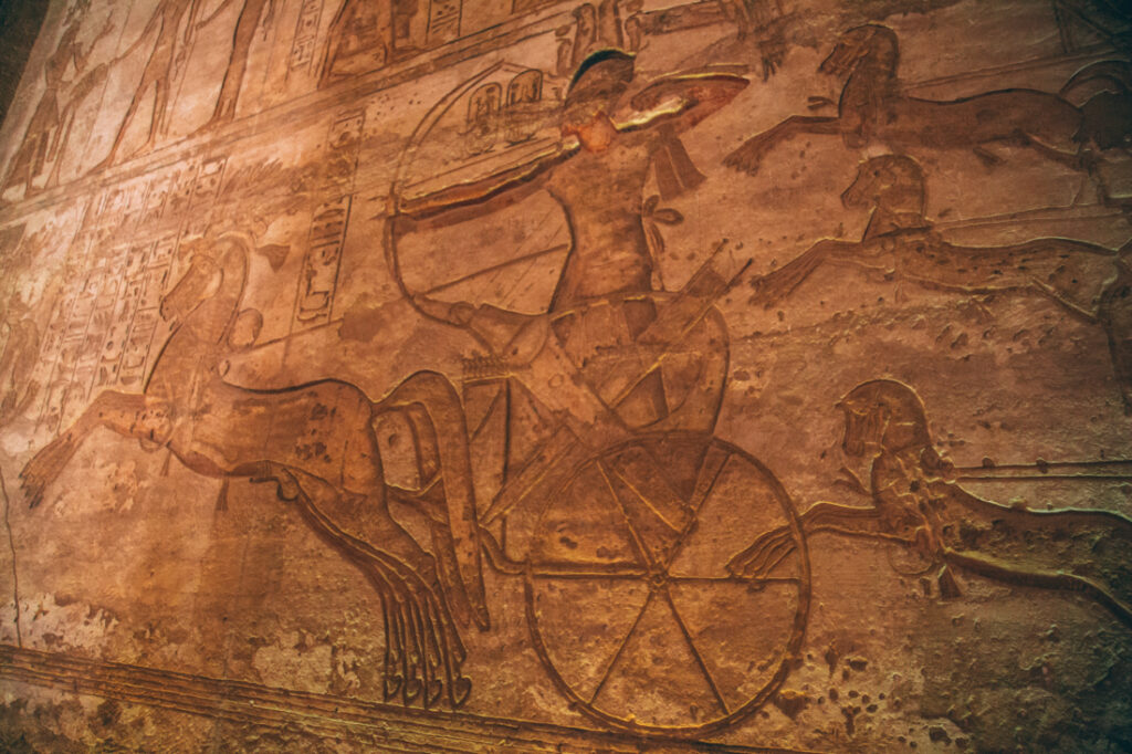 A close up image of a wall carving inside an Abu Simbel depicting a pharaoh riding on a carriage.