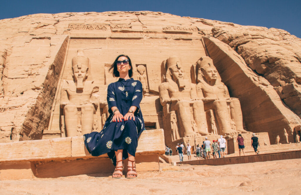 Women with short hair wearing a modest maxi dress and posing in front of Nefertari's temple at Abu Simbel, Egypt