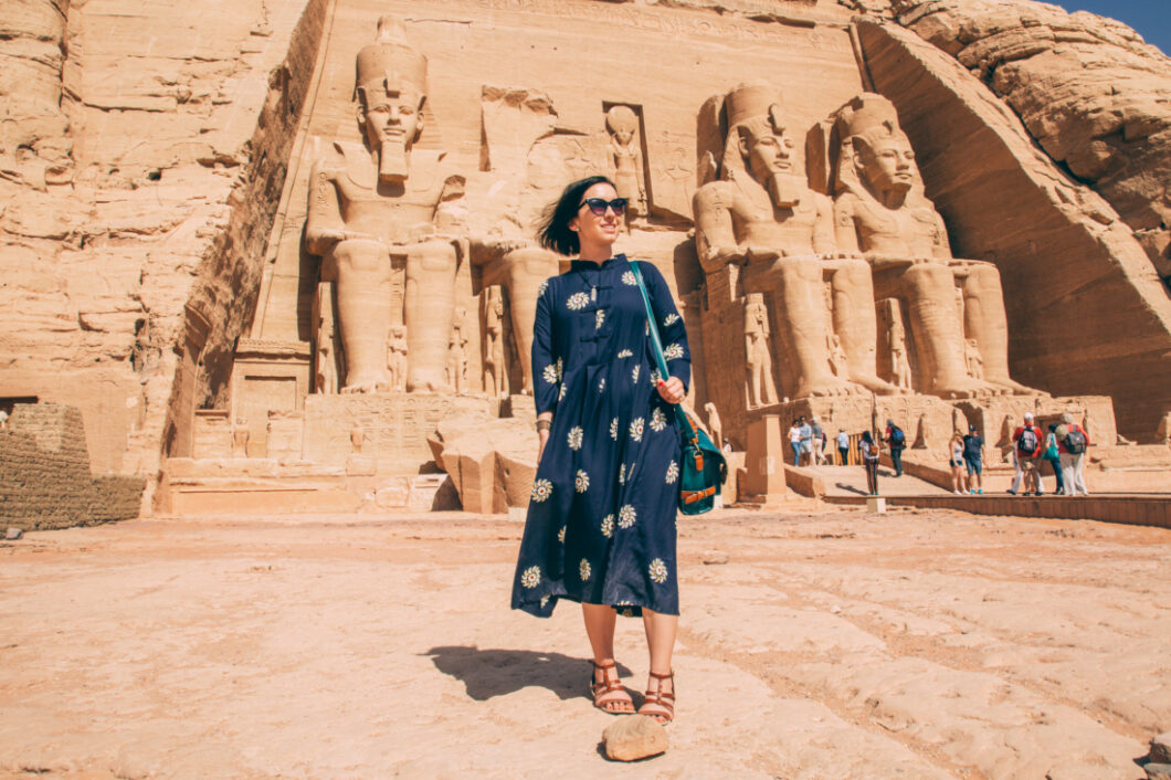 A woman in a blue dress standing in front of a statue of an ancient Egyptian pharaoh in Abu Simbel.