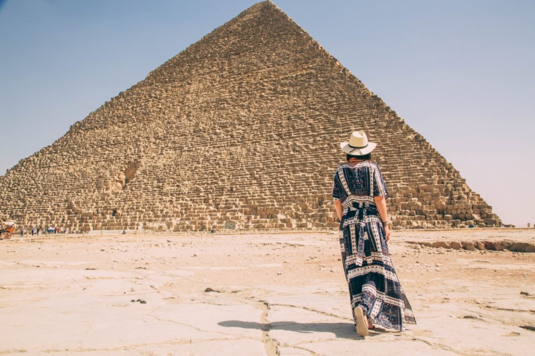 A woman in a dress is standing in front of a pyramid.