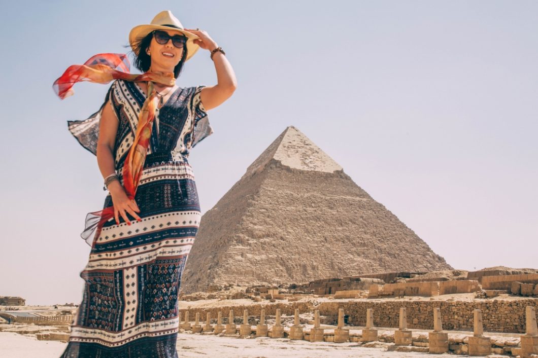 A woman in a dress and scard standing in front of the pyramids.