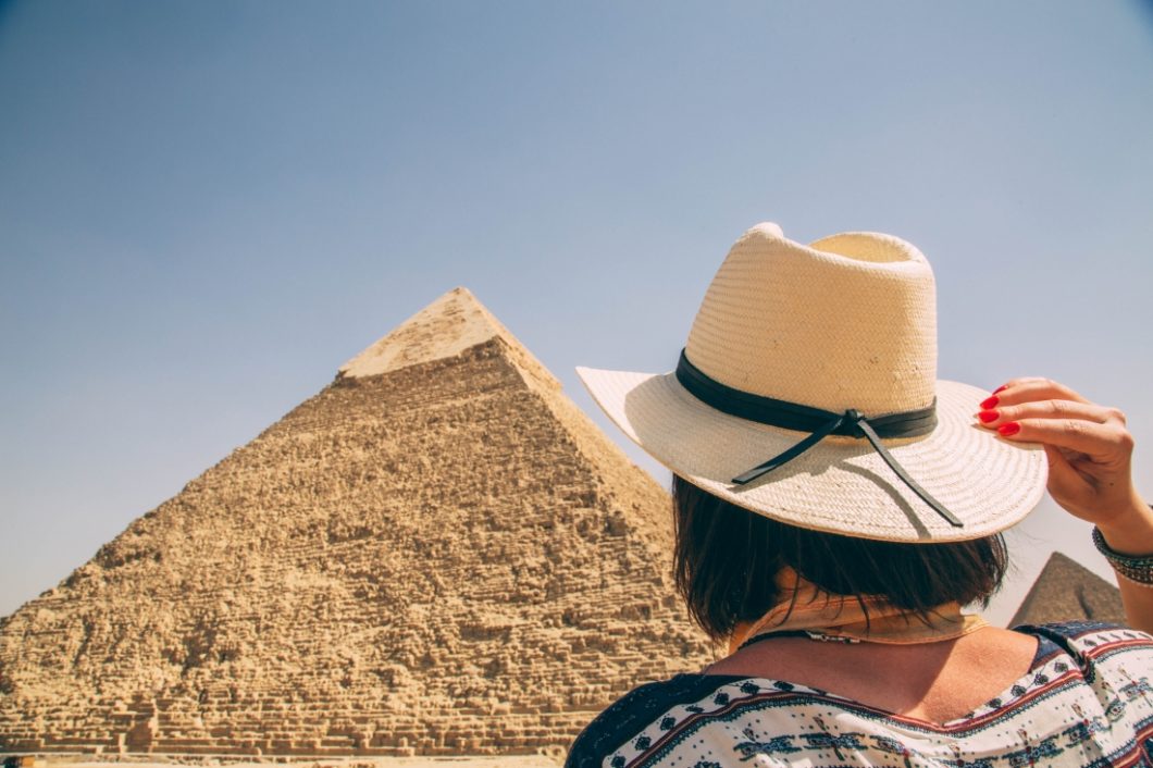 A woman wearing a hat in front of the pyramids of Giza.