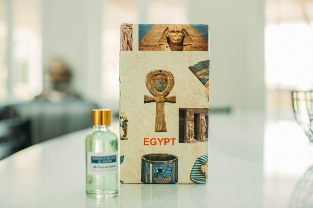 A bottle of essential oil on a white table with a box on the side with Egypt written on it. 