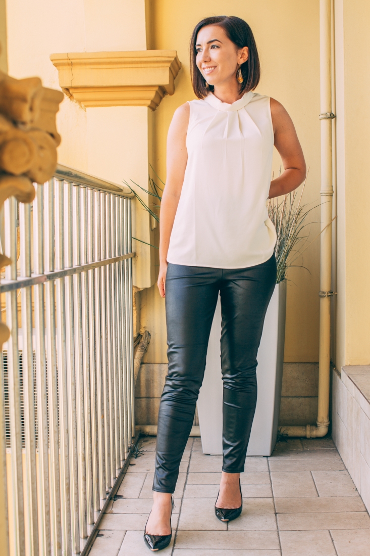 lindsey wearing a cream sleeveless tunic with black leather leggings and black patent leather pumps standing on balcony