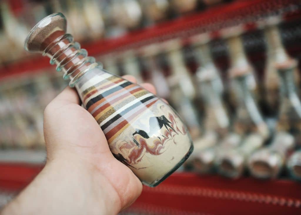 A person holding a glass sand souvenir bottle from Egypt in their hand.