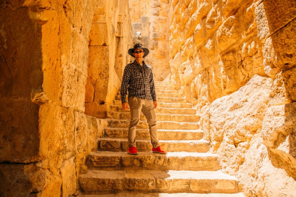 Zac wearing a button down and hiking pants standing on stone stairs in Jordan