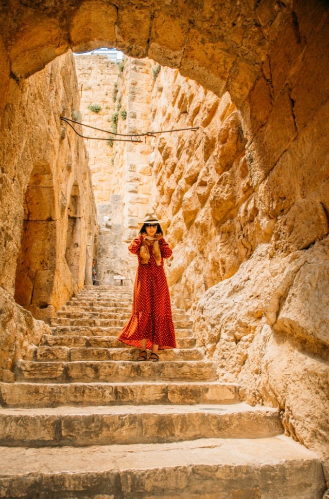 A woman in a red dress standing on a stone staircase in Ajloun Castle, Jordan.