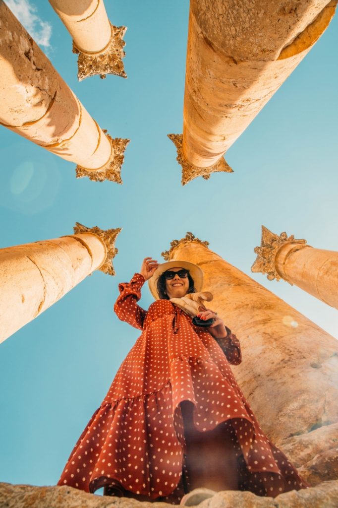 A woman in a red dress standing in front of columns in Jerash.