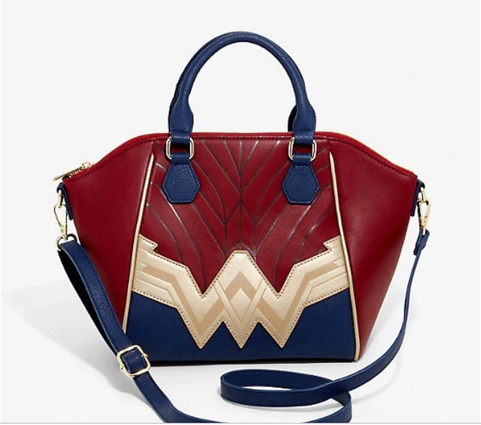 This crossbody bag is a red leather bag with a gold leather Wonder Woman logo across the front. The bag has navy blue leather handles.